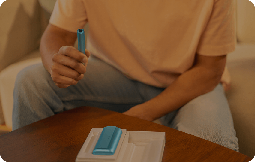 A person interacting with IQOS device in a casual indoor setting.