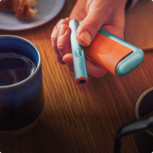 Eine Hand hält ein IQOS mit Accessoires ausgestattet.