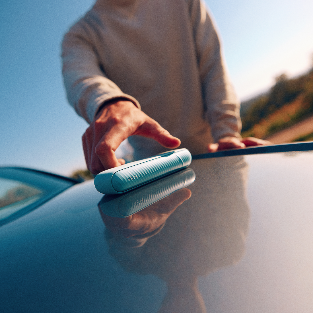 Persona sosteniendo IQOS Iluma i turquesa sobre la superficie de un automóvil