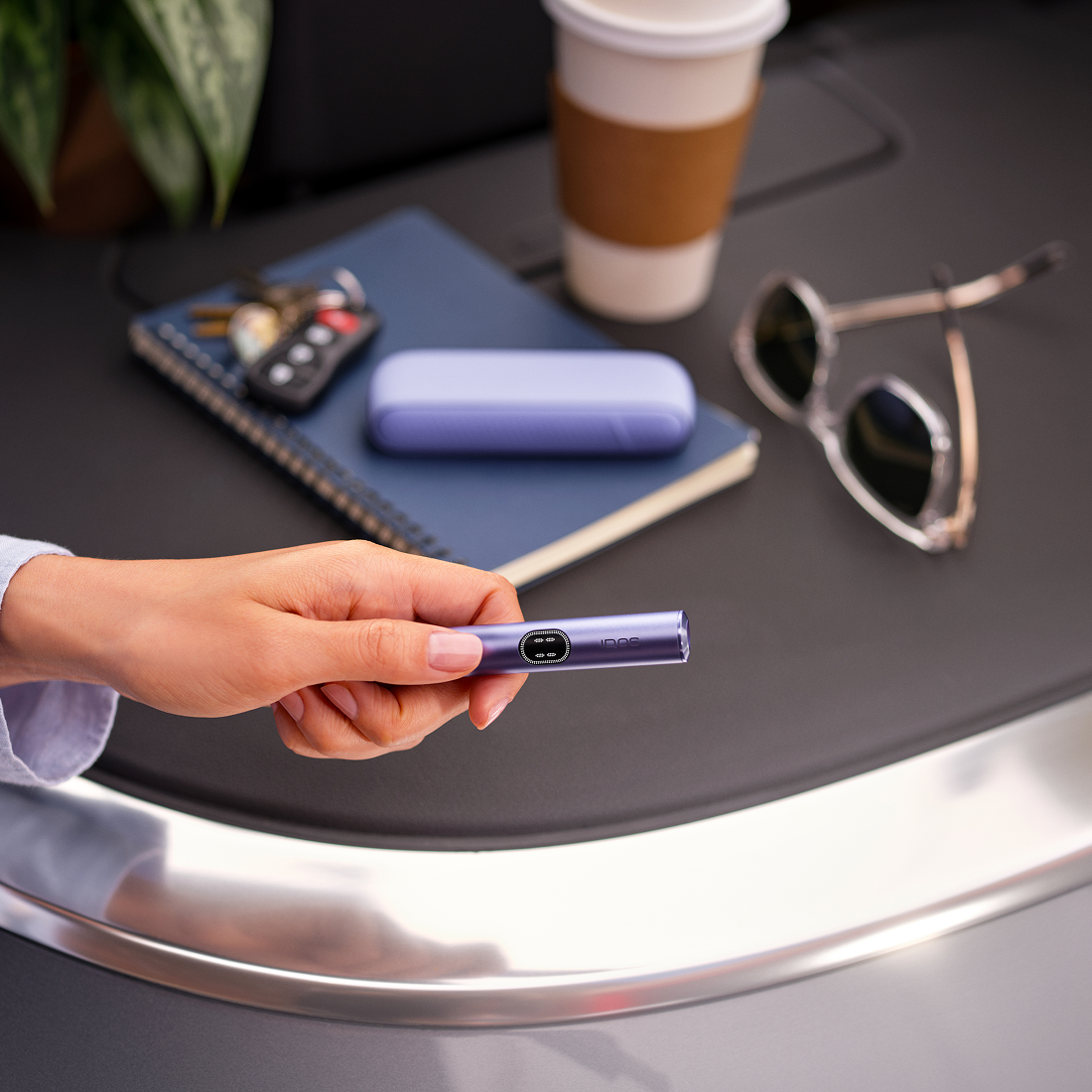 Persona usando IQOS Iluma i turquesa sobre charola metálica junto a taza de café