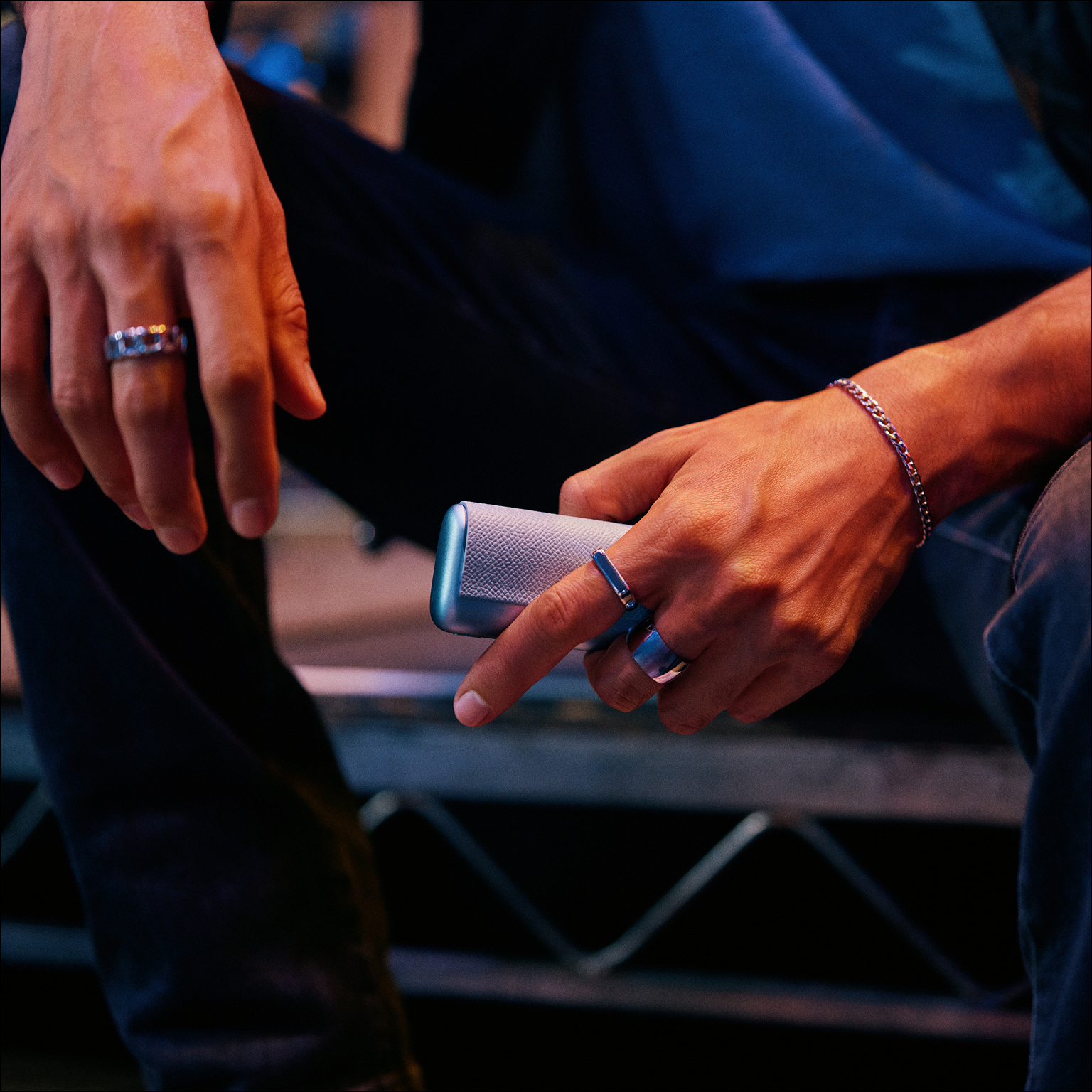 Persona sentada en una tarima backstage usando un IQOS ILUMA i turquesa.