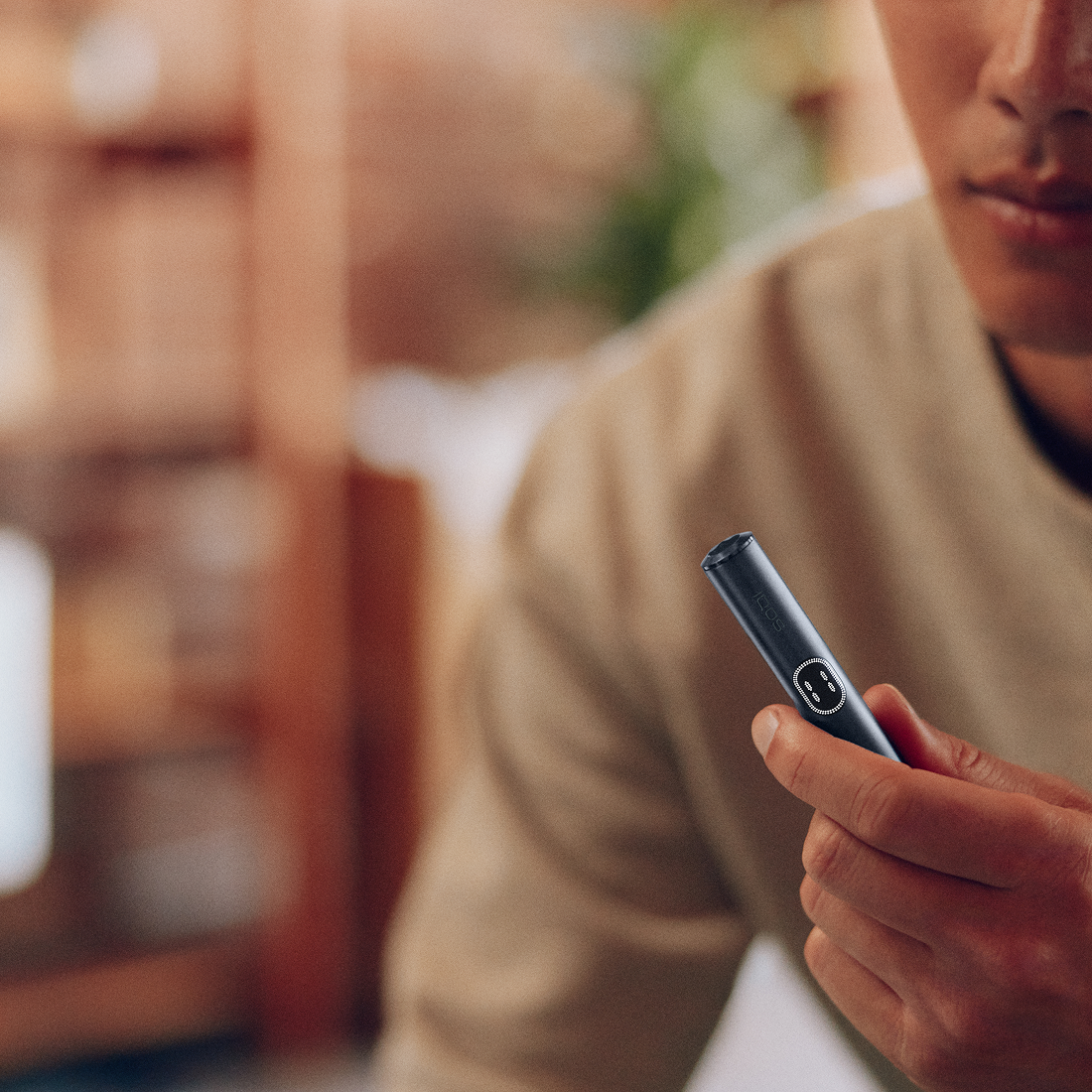 Hombre revisando IQOS Iluma i turquesa en interior con fondo cálido