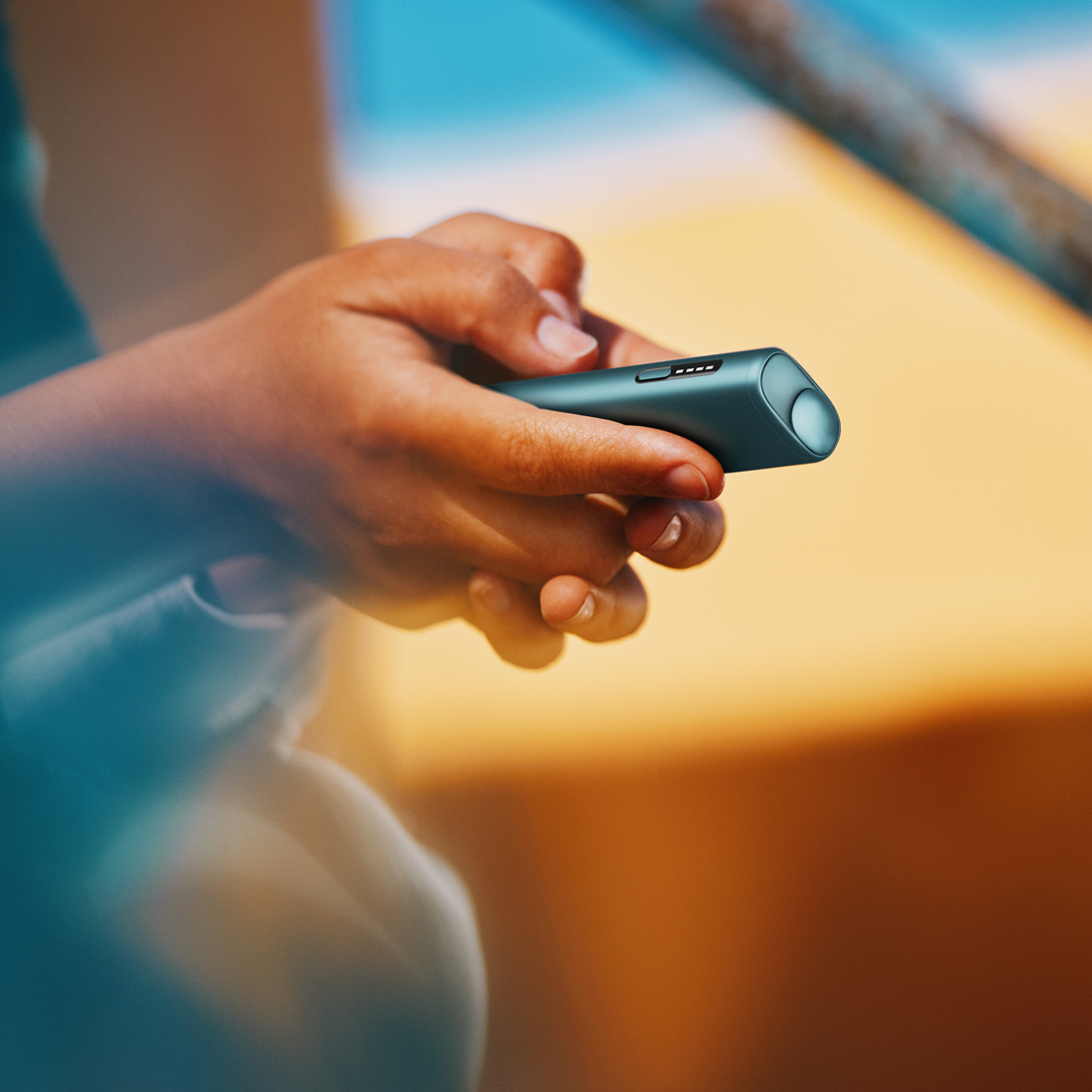 Persona usando IQOS Iluma i turquesa en ambiente soleado sosteniéndolo con ambas manos