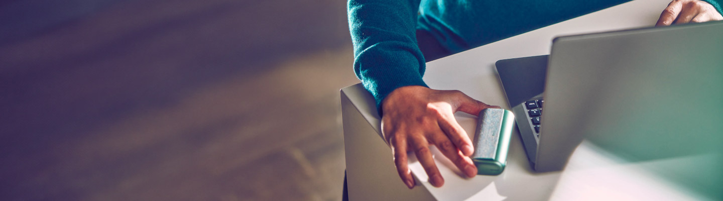 A man picks up the IQOS ILUMA device located to the left of his laptop.