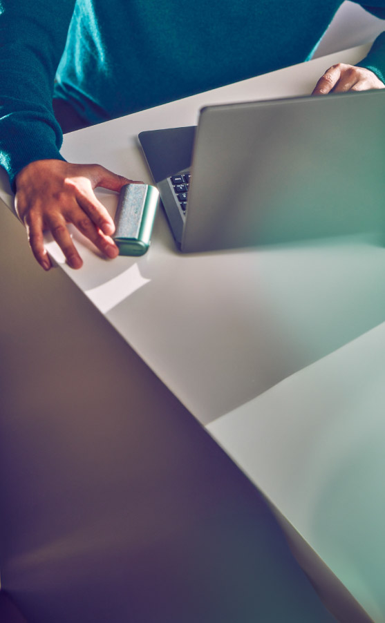 A man picks up the IQOS ILUMA device located to the left of his laptop.