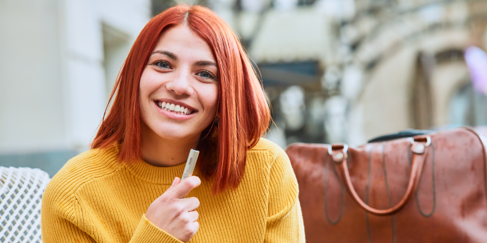 Usměvavé žena s IQOS ILUMA v pozadí cestovní taška