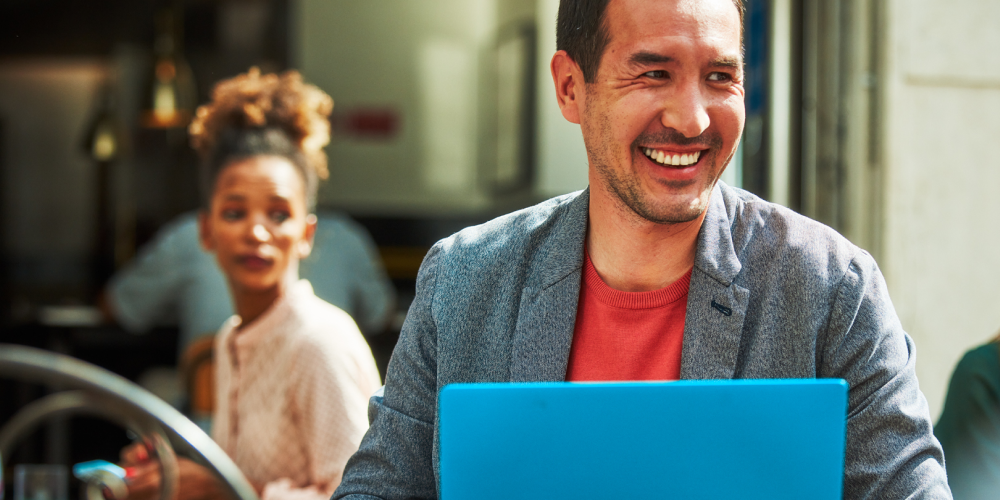 Muž sedící v kavárně s laptopem v pozadí žena dívající se jeho směrem