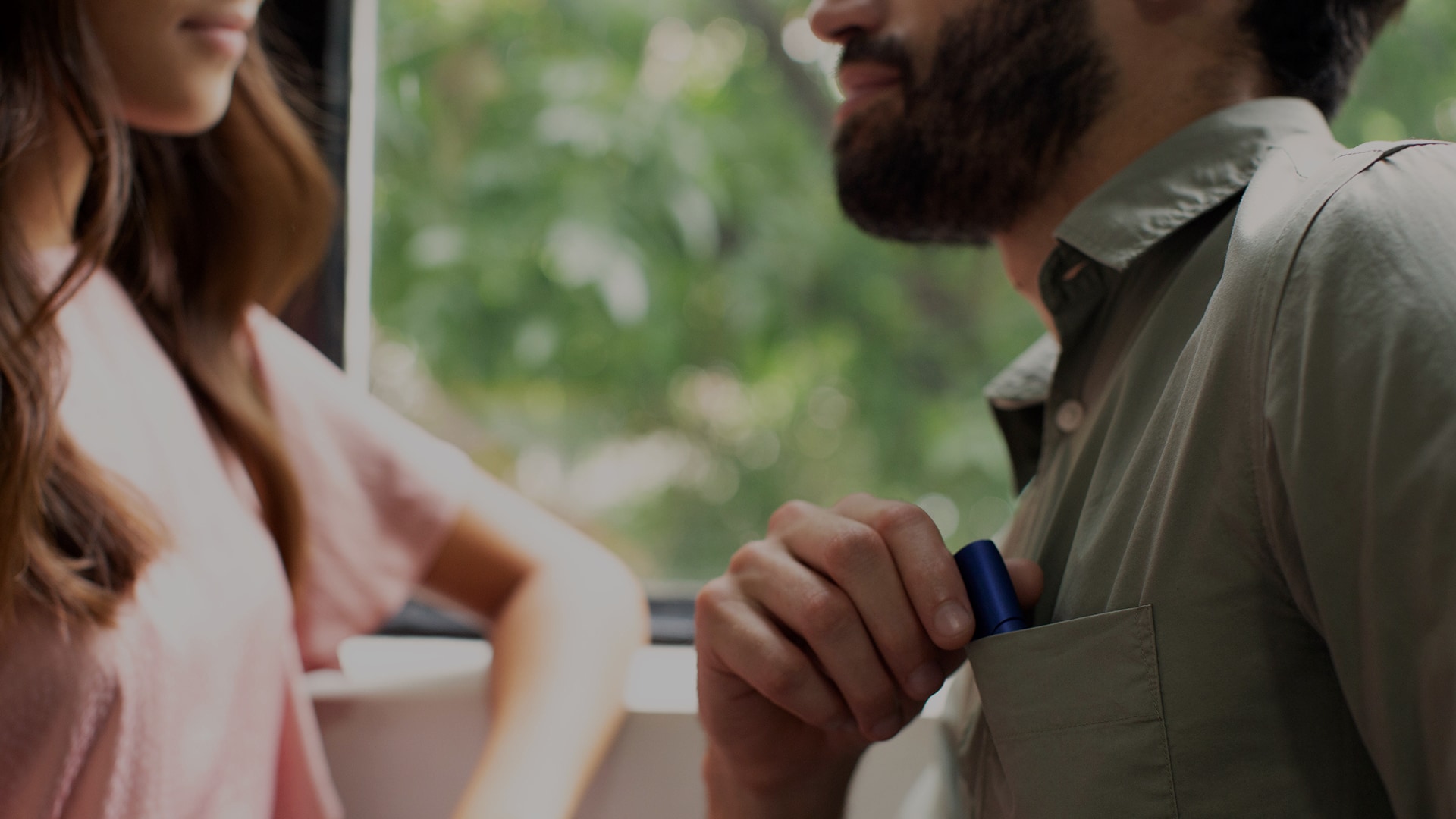 A close-up of two people, the man is reaching into his shirt pocket for his IQOS 3 device