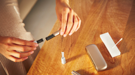 Woman opening her IQOS holder with the charger and other accessories on a table