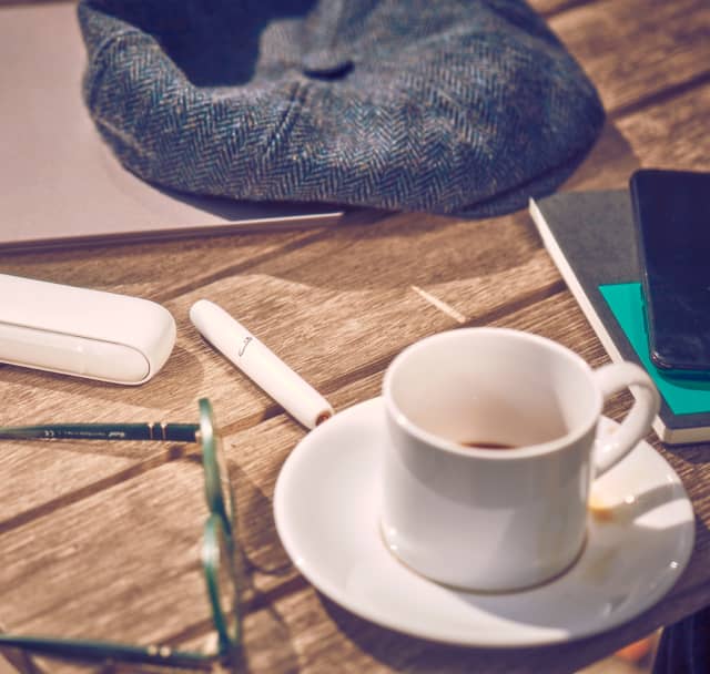 IQOS 3 DUO on a table next to a cup of coffee.