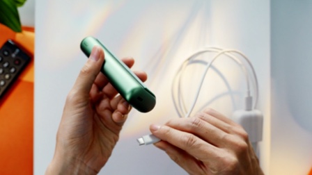 Hands plugging an IQOS ILUMA ONE into a power adaptor.