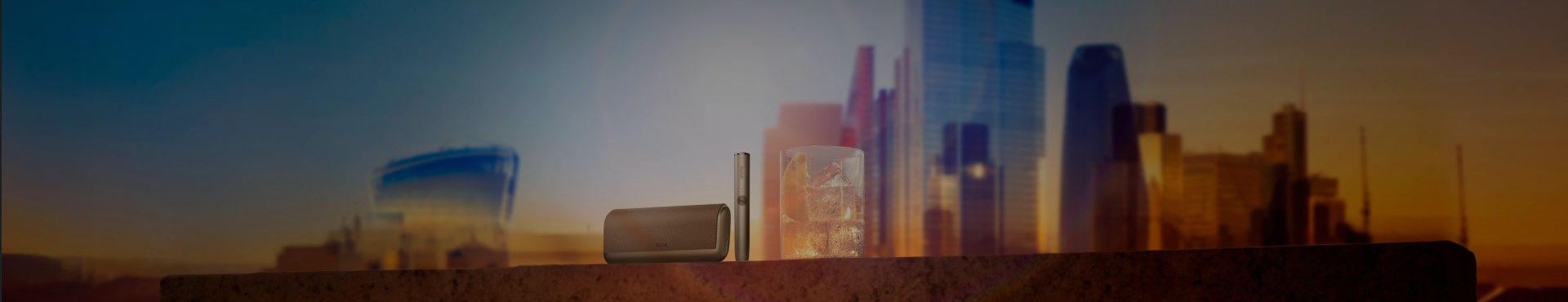 A cityscape at sunset with a clear sky, featuring tall buildings and skyscrapers with a warm orange glow on the horizon.